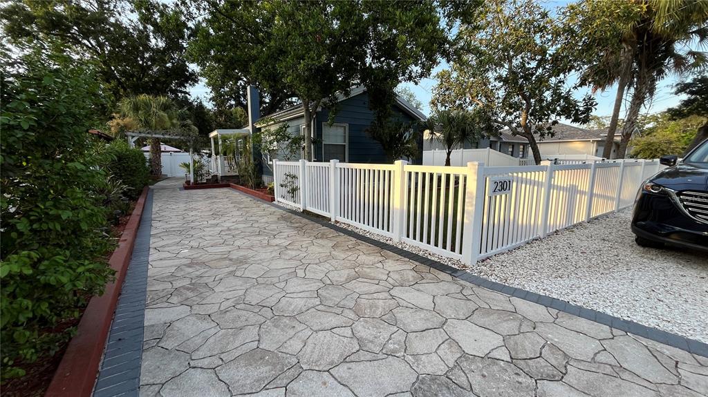 A stone-paved driveway leads to a blue house enclosed by a white picket fence — 2301 W IDLEWILD AVENUE, TAMPA, FL