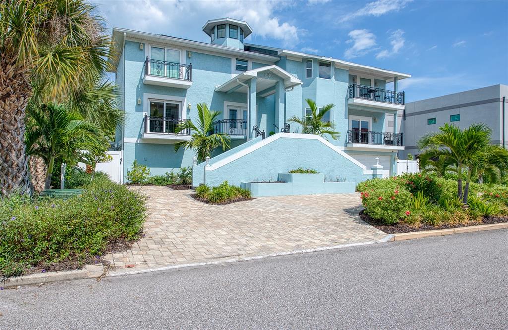 A three-story light blue house with balconies and a paved driveway under a blue sky — 289 8TH AVENUE N, TIERRA VERDE, FL