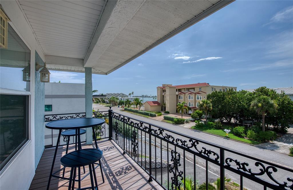 A balcony with a small table and chairs overlooks a street, trees, and distant water — 289 8TH AVENUE N, TIERRA VERDE, FL