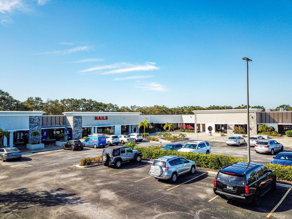 An exterior view of a commercial strip mall with a parking lot under a blue sky — 7421 MANATEE AVENUE W UNIT 7457, BRADENTON, FL