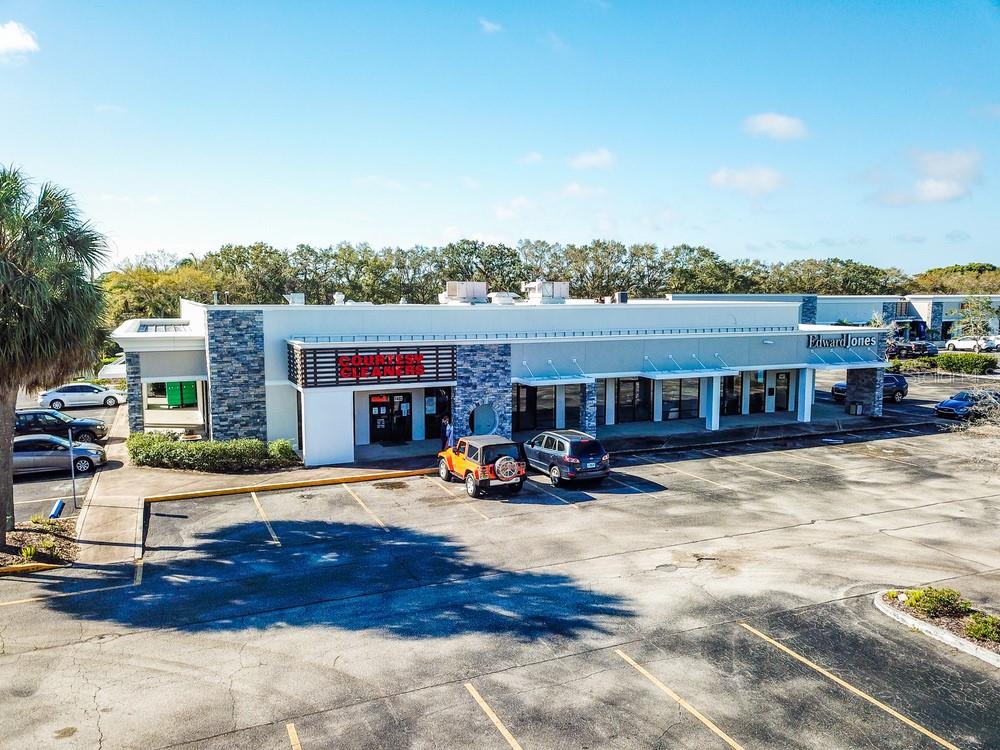 An aerial view of a commercial strip mall with a parking lot and several vehicles — 7421 MANATEE AVENUE W UNIT 7457, BRADENTON, FL