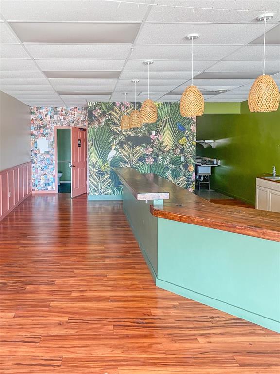 A commercial space features a wooden bar, tropical wallpaper, pendant lighting, and wood-look flooring — 7421 MANATEE AVENUE W UNIT 7457, BRADENTON, FL