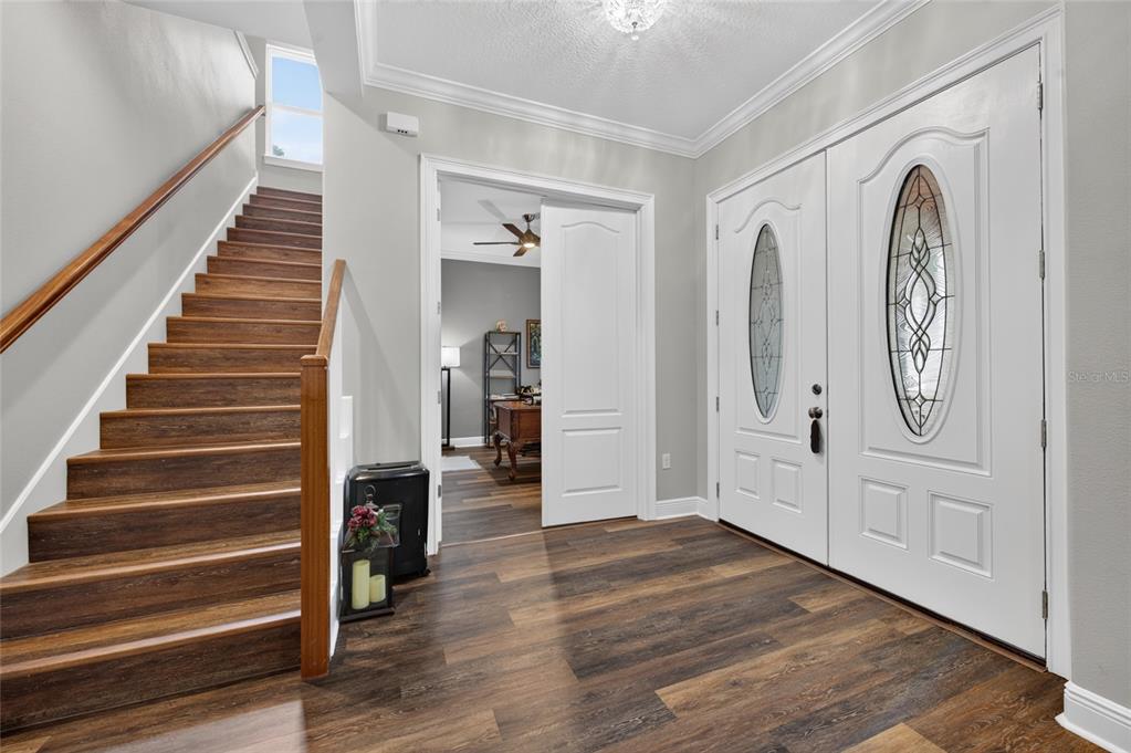 An entryway features wood-look flooring, a staircase with a wooden railing, and white double doors — 1515 RAMBLING OAKS LANE, DELAND, FL