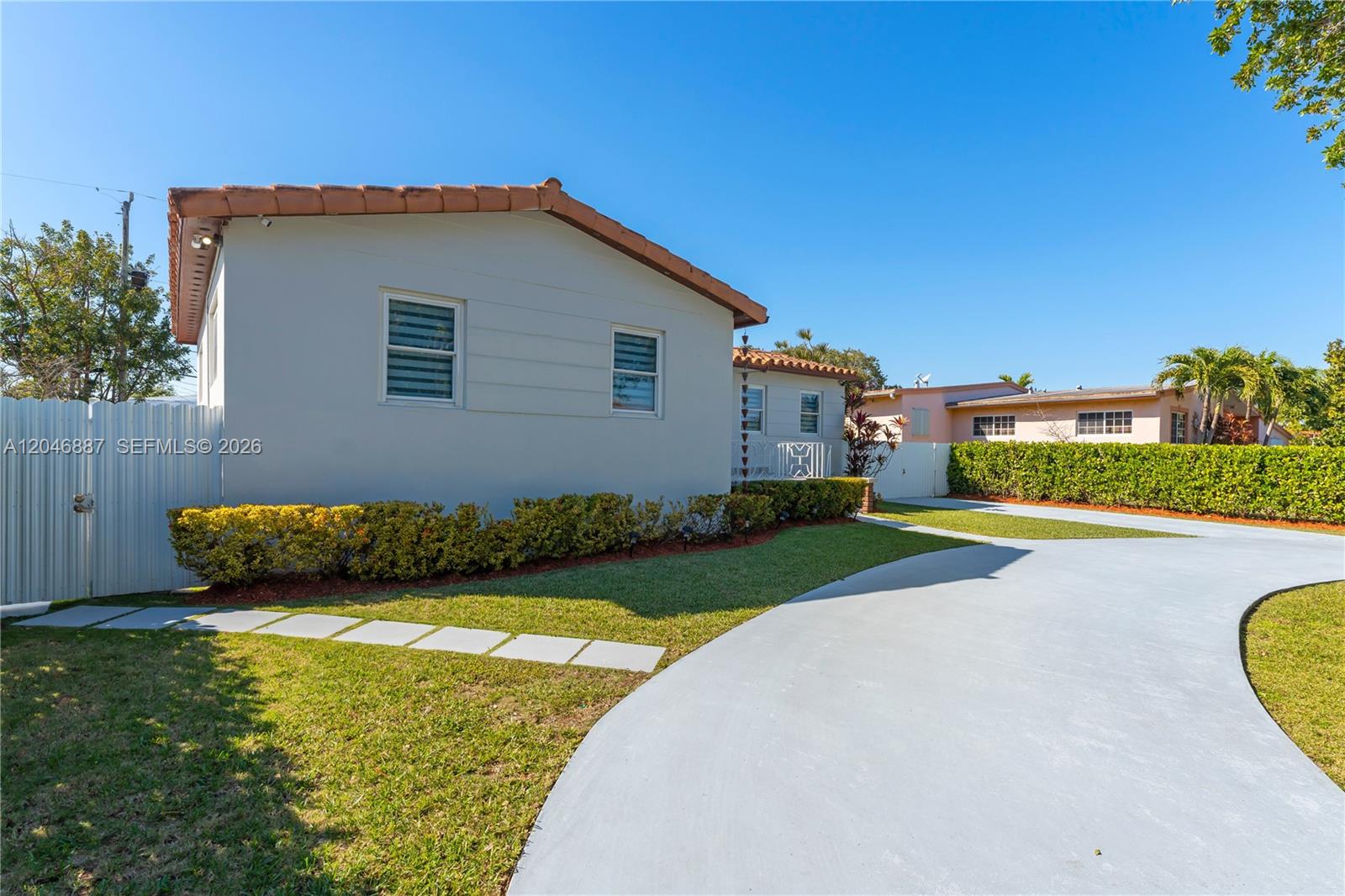 A light-colored house with a tiled roof features a curved driveway and manicured landscaping — MIAMI, FL