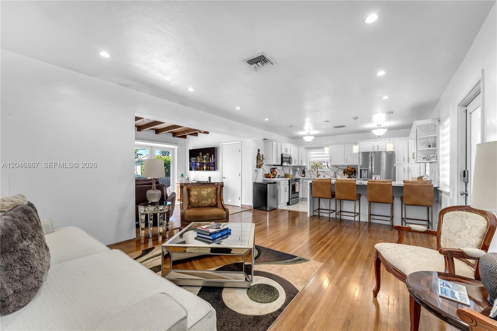 An open-concept living room and kitchen feature hardwood floors, white cabinetry, and a breakfast bar — MIAMI, FL