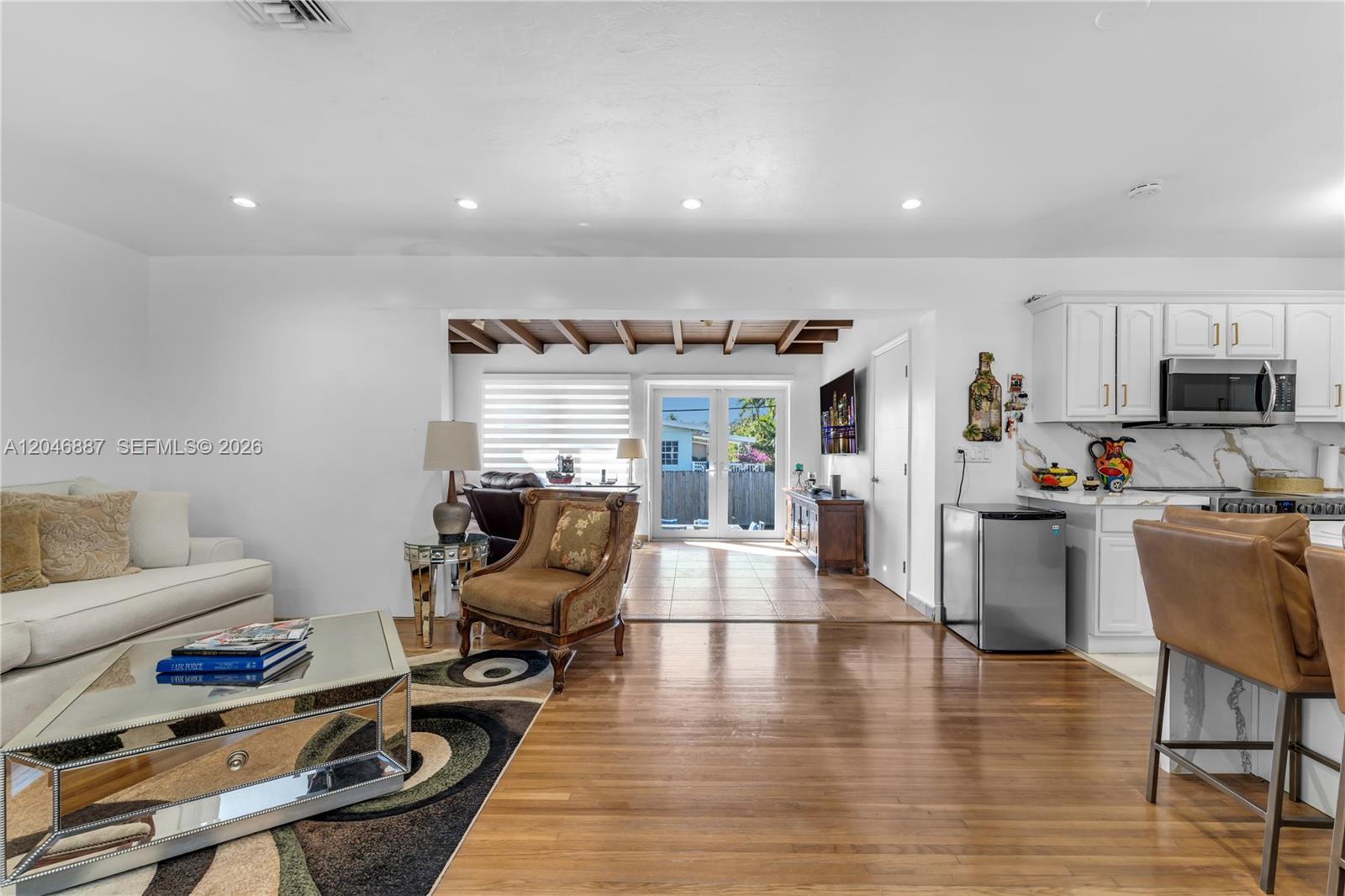 A living room with hardwood floors, a mirrored coffee table, and an adjacent kitchen area — MIAMI, FL
