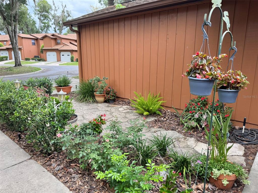 A stone patio sits beside a brown house with hanging planters and various potted plants — 2701 NE 10TH STREET UNIT 401, OCALA, FL