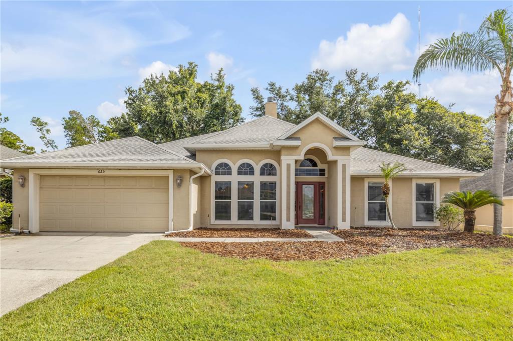 A single-story tan house with a two-car garage, arched windows, and a front entryway — 625 QUAIL LAKE DRIVE, DEBARY, FL