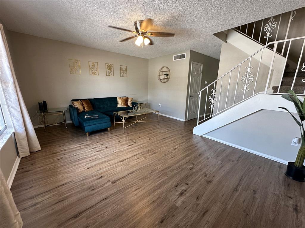 A living room features wood-look flooring, a blue sectional sofa, and a staircase with railings — 6060 VILLAGE CIRCLE UNIT 6060, ORLANDO, FL