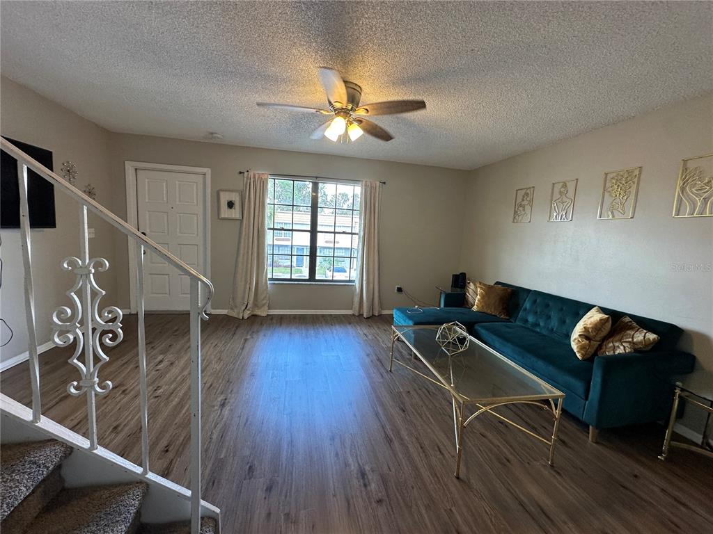 A living room features wood-look flooring, a teal sectional sofa, and a white staircase railing — 6060 VILLAGE CIRCLE UNIT 6060, ORLANDO, FL
