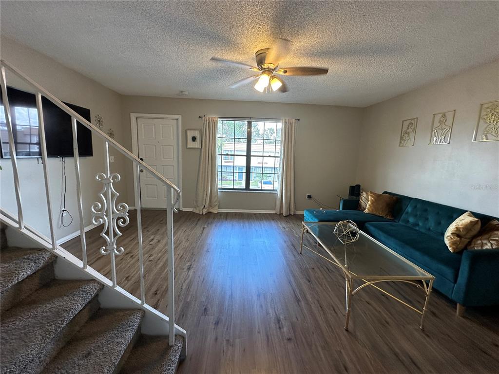 A living room features wood-look flooring, a teal sectional sofa, and a staircase with railing — 6060 VILLAGE CIRCLE UNIT 6060, ORLANDO, FL