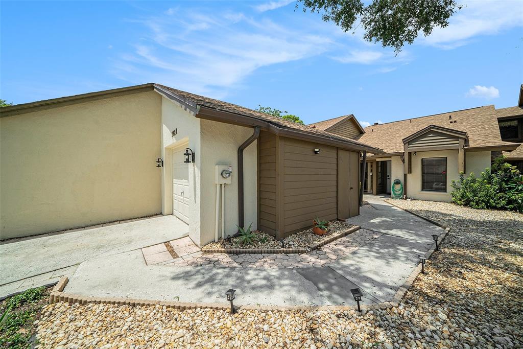 A beige house exterior features a garage, a brown storage shed, and a gravel yard — 1923 BAYSHORE COURT, SAFETY HARBOR, FL