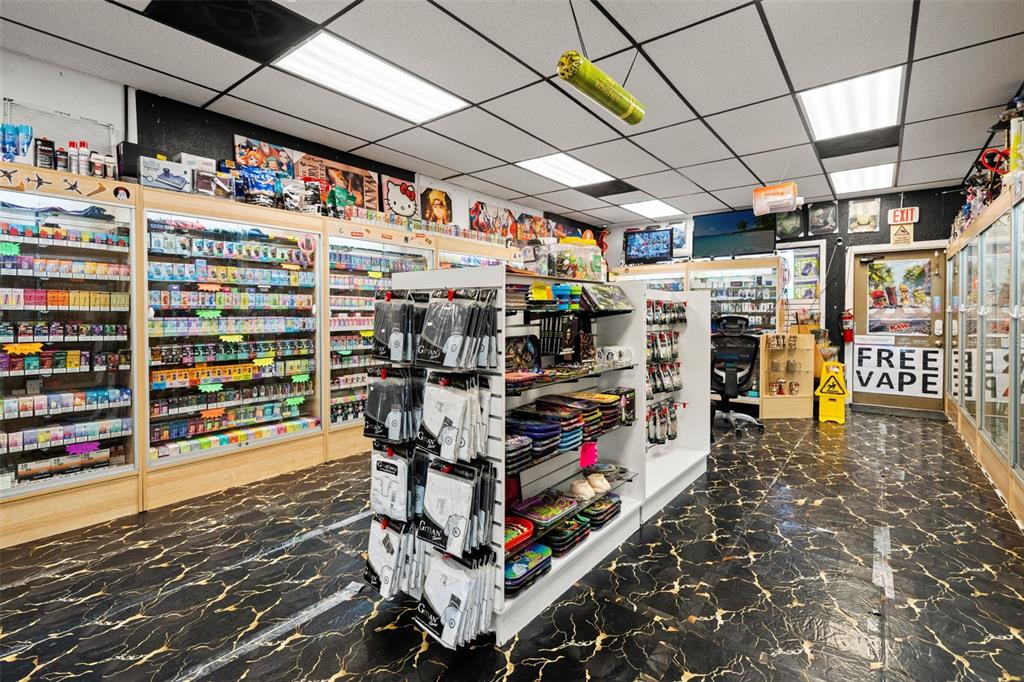 A retail shop interior features glass display cases, merchandise shelving, and black marble-patterned flooring — 49TH STREET, PINELLAS PARK, FL