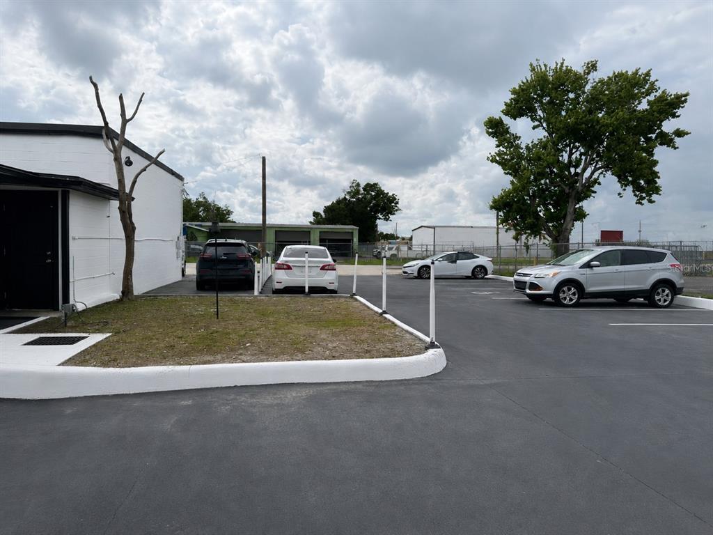 A paved parking lot with several parked cars sits beside a white building and tree — 607 FAIRVILLA ROAD, ORLANDO, FL