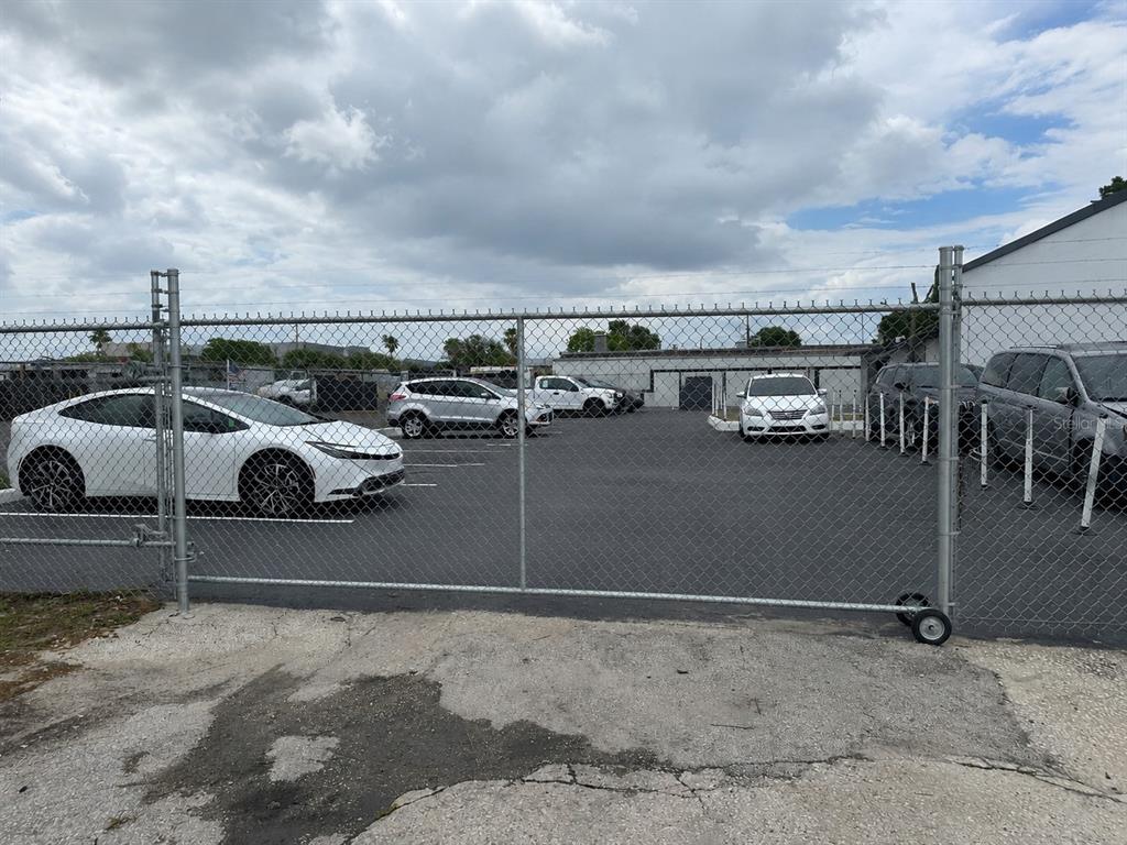 A chain-link fence encloses a paved parking lot with several cars parked in front of buildings — 607 FAIRVILLA ROAD, ORLANDO, FL