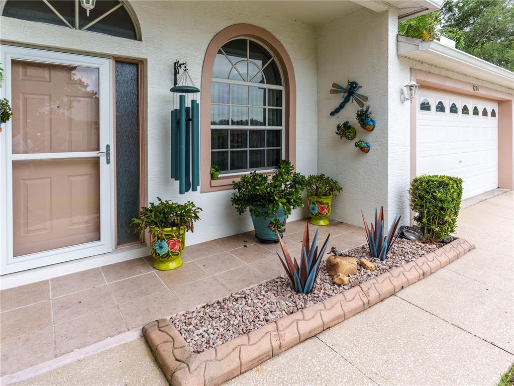 A front porch features potted plants, metal agave sculptures, and a stone-bordered gravel garden bed — 9234 SANTA MONICA WAY, NEW PORT RICHEY, FL