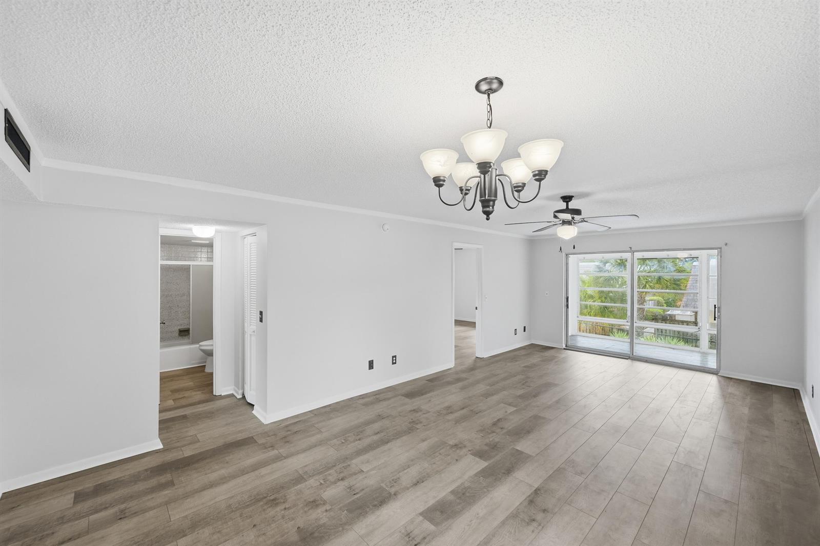 An empty living room with light wood-look flooring, a chandelier, ceiling fan, and sliding doors — 1166 6th Avenue # B8, Vero Beach FL 32960, VERO BEACH, FL