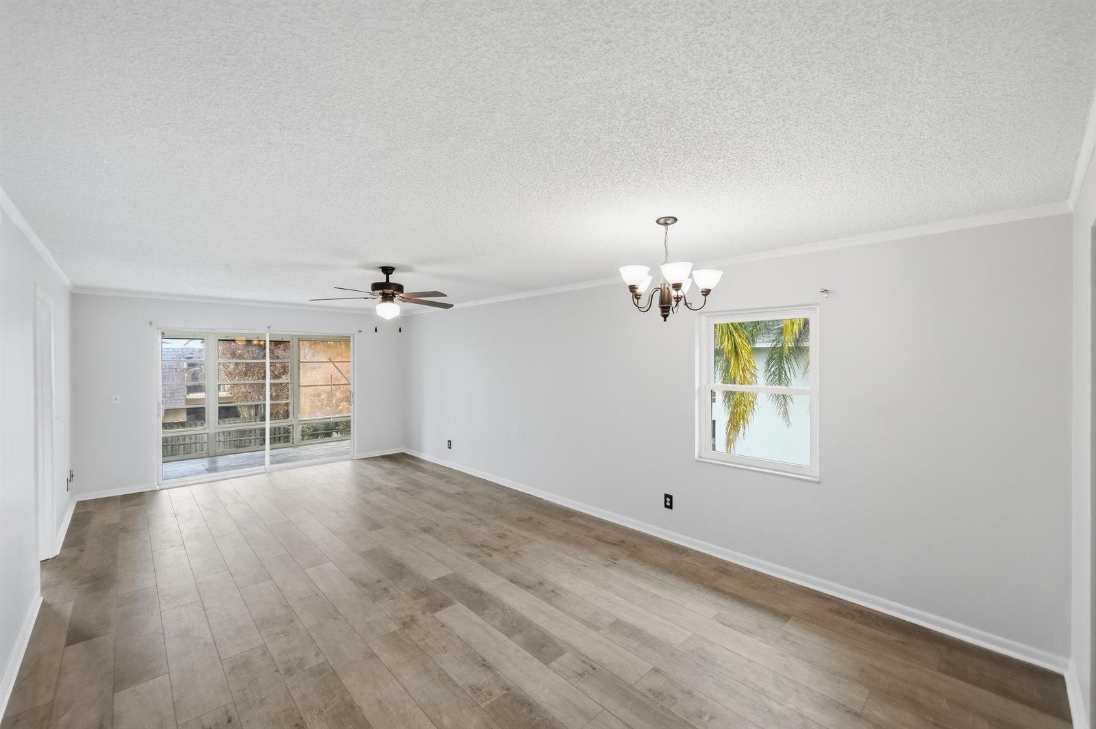 An empty living room features light wood-look flooring, a ceiling fan, and a chandelier — 1166 6th Avenue # B8, Vero Beach FL 32960, VERO BEACH, FL