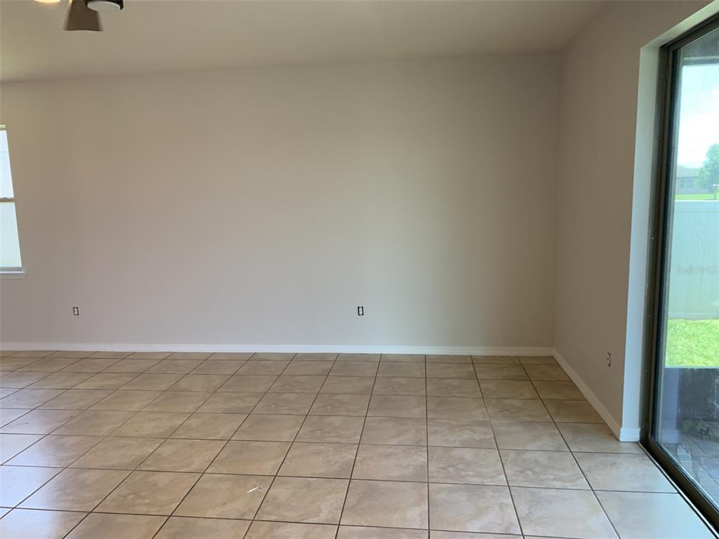 An empty room with beige walls, tan tile flooring, and a sliding glass door — 3966 BAJA DRIVE, ST CLOUD, FL