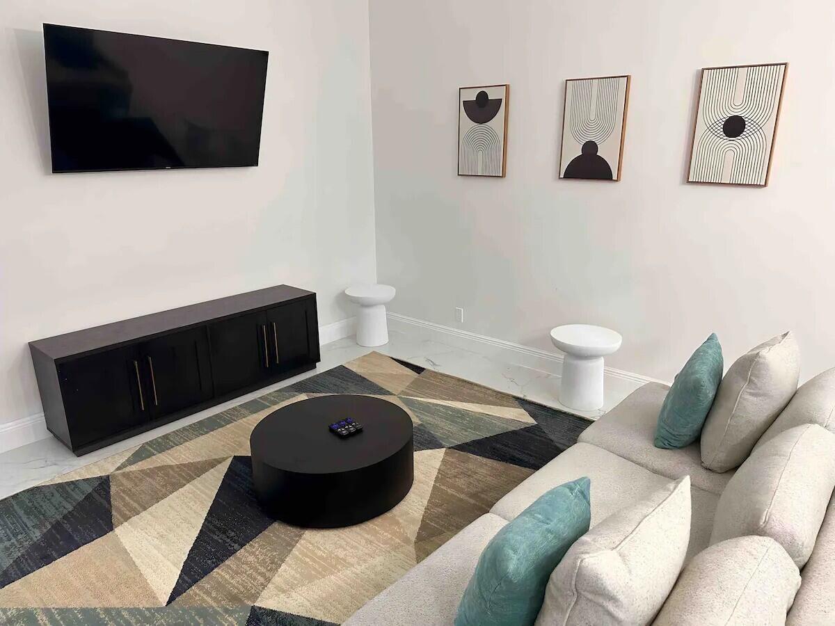 A modern living room features a wall-mounted television, a black media console, and geometric art — 1255 PERIWINKLE Place, Wellington FL 33414, WELLINGTON, FL