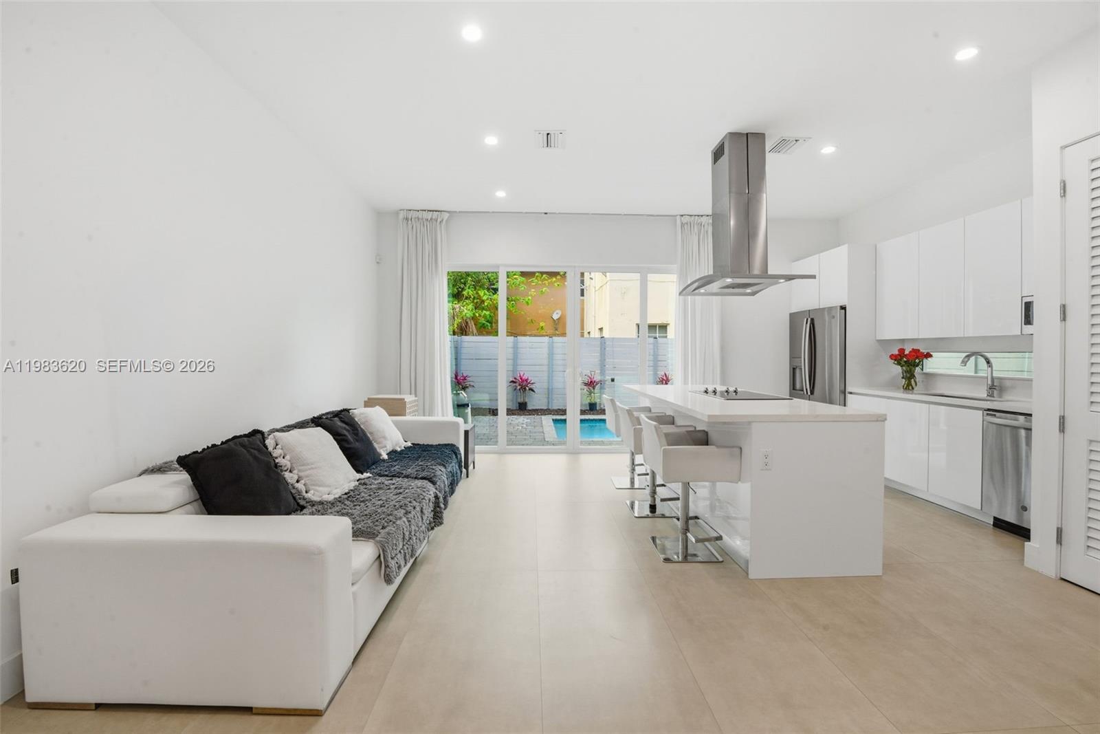A modern open-concept kitchen and living area features white cabinetry, a central island, and pool views — 3525 Day Ave, Miami FL 33133, MIAMI, FL