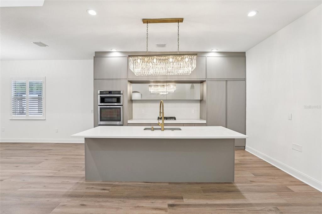 A modern kitchen features a large white island, gray cabinetry, and a crystal chandelier — 10409 ANGEL OAK COURT, ORLANDO, FL
