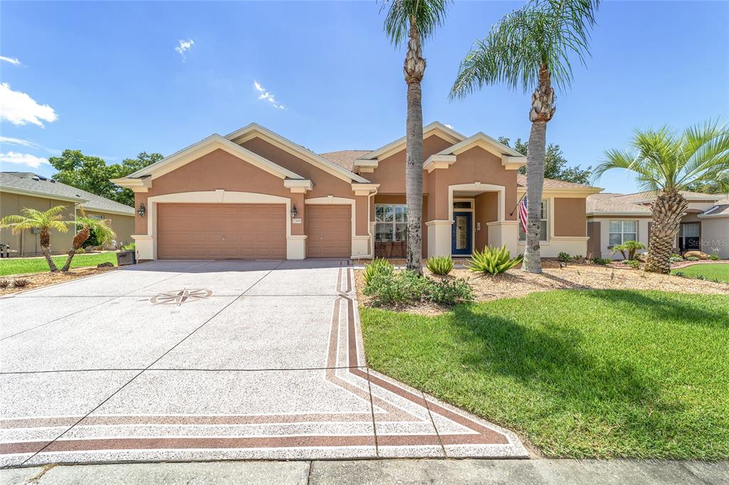 A single-story house with a tan stucco exterior, a three-car garage, and two palm trees — 12859 SE 91ST TERRACE ROAD, SUMMERFIELD, FL