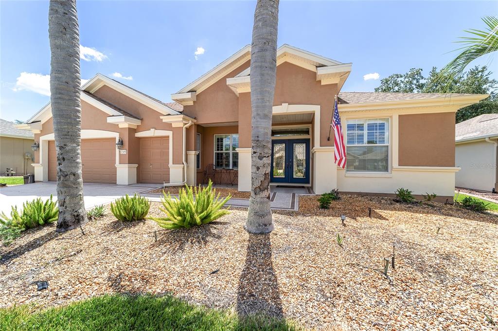 A tan single-story house with a two-car garage, palm trees, and a gravel front yard — 12859 SE 91ST TERRACE ROAD, SUMMERFIELD, FL