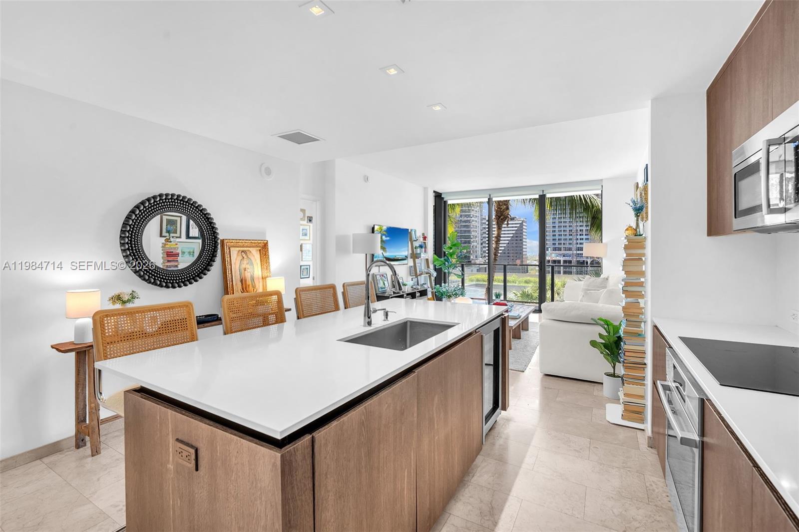 A modern kitchen features a large white island with a sink and wood cabinetry — 68 SE 6th St # 806, Miami FL 33131, MIAMI, FL