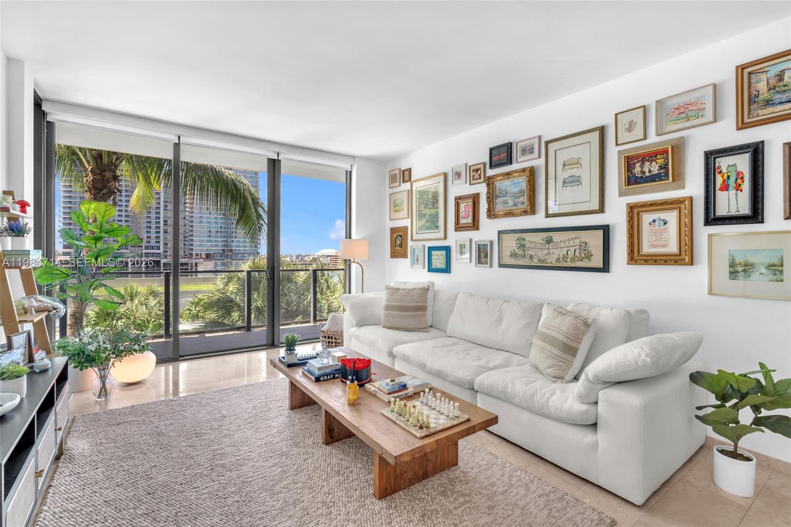 A living room features a white sofa, a wooden coffee table, and a gallery wall — 68 SE 6th St # 806, Miami FL 33131, MIAMI, FL