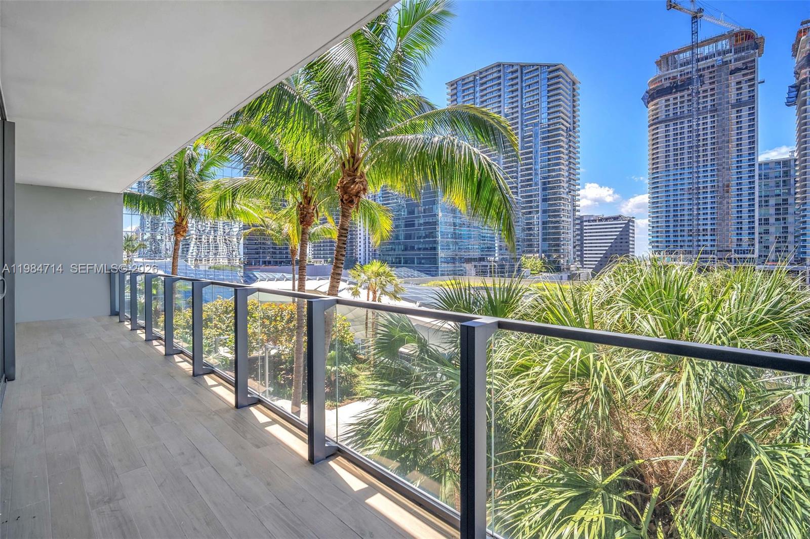 A balcony with wood-look tile flooring overlooks palm trees and urban high-rise buildings — 68 SE 6th St # 806, Miami FL 33131, MIAMI, FL