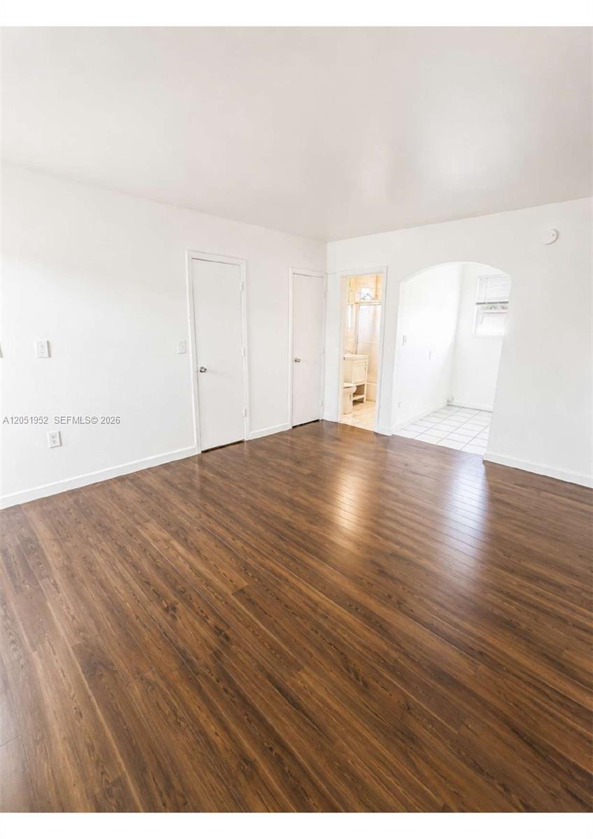 An empty room features wood-look flooring, white walls, two closed doors, and an arched entryway — 5305 Biscayne Blvd # 203, Miami FL 33137, MIAMI, FL