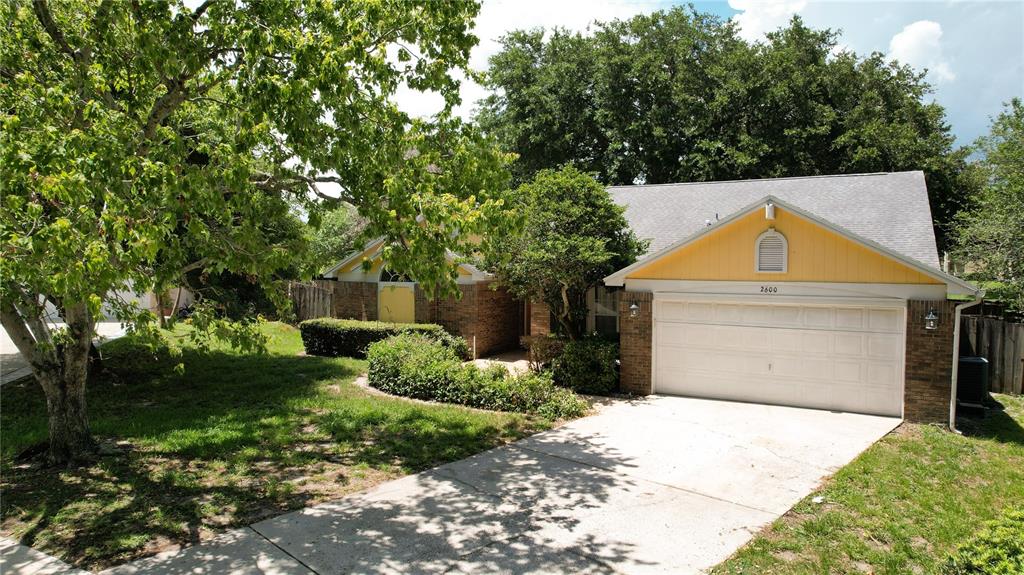 A brick and yellow-sided house features a two-car garage and a large front tree — 2600 CLEMENTON PARK COURT, ORLANDO, FL