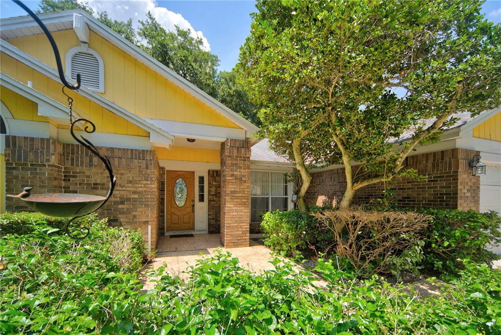 The exterior of a yellow house features a brick facade, a front porch, and landscaping — 2600 CLEMENTON PARK COURT, ORLANDO, FL