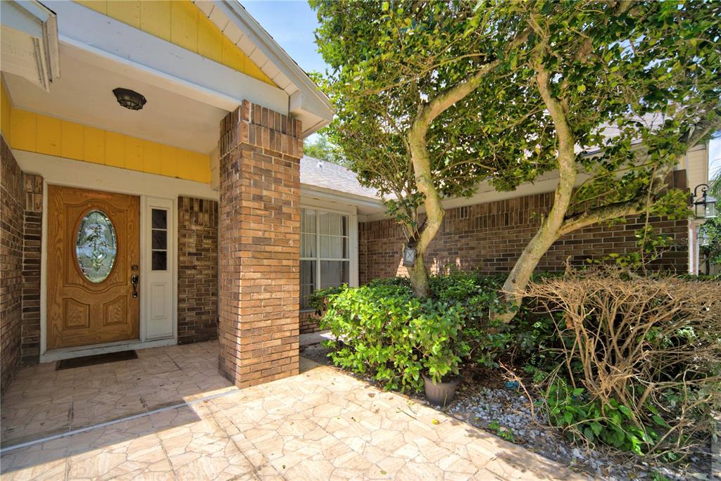 A brick house exterior features a wooden front door, a tiled porch, and a large tree — 2600 CLEMENTON PARK COURT, ORLANDO, FL