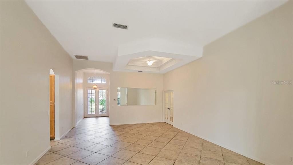 A spacious living room features a tray ceiling, tile flooring, and a large wall mirror — 6836 BAY HILL DRIVE, LAKEWOOD RANCH, FL