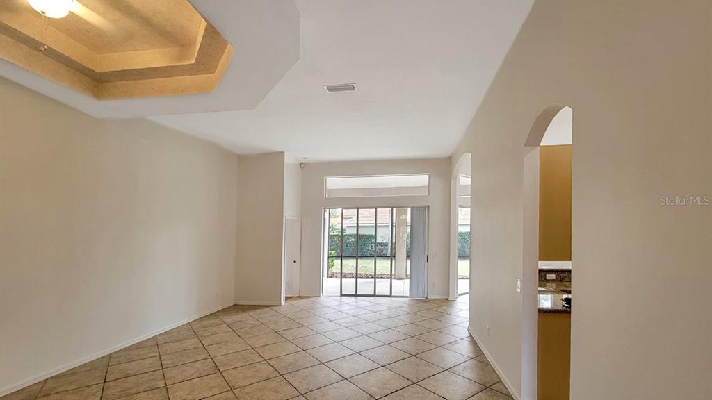 An empty living room with tile floors, a tray ceiling, and sliding glass patio doors — 6836 BAY HILL DRIVE, LAKEWOOD RANCH, FL