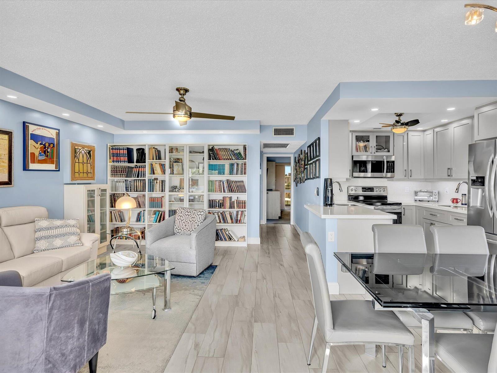 An open-concept living room and kitchen featuring light blue walls, bookshelves, and tile flooring — 4038 Swansea B, Deerfield Beach FL 33442, DEERFIELD BEACH, FL