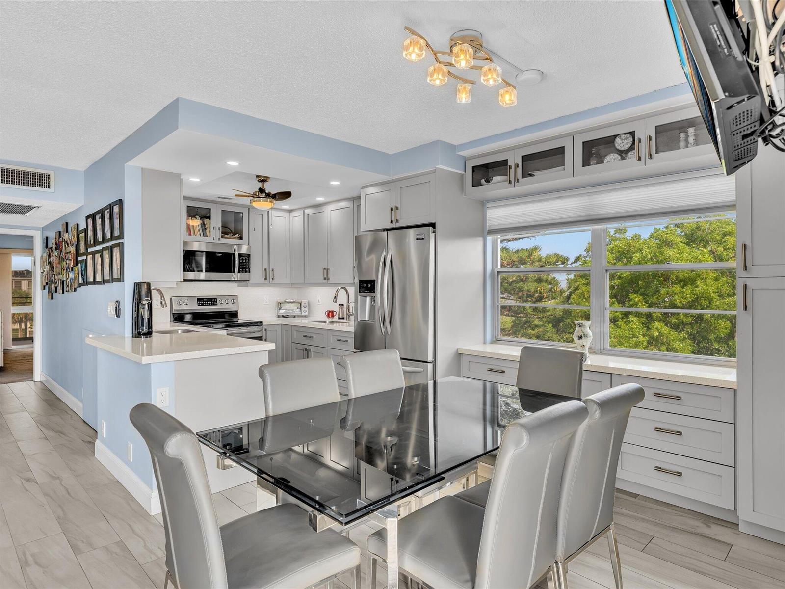 A dining area with a glass table and grey chairs adjacent to a modern kitchen — 4038 Swansea B, Deerfield Beach FL 33442, DEERFIELD BEACH, FL