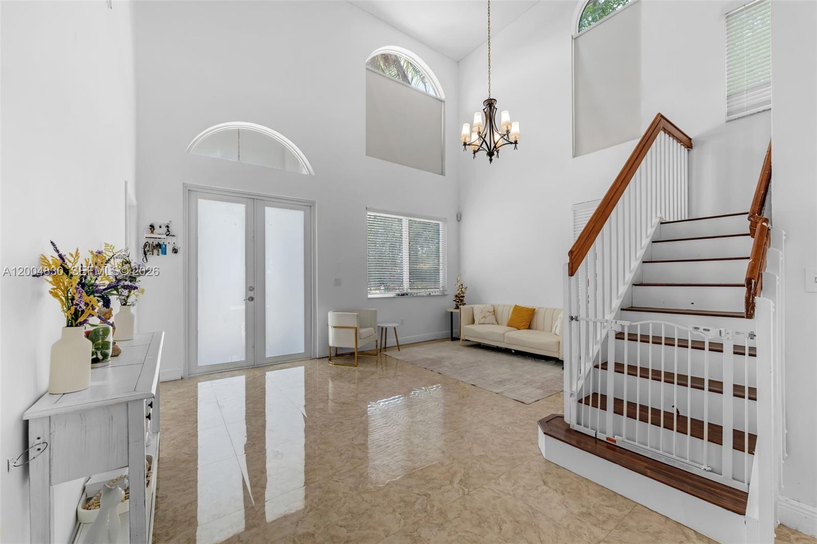 A bright, high-ceilinged foyer features marble-look tile floors, a wooden staircase, and a chandelier — 13891 SW 39th Ter, Miami FL 33175, MIAMI, FL