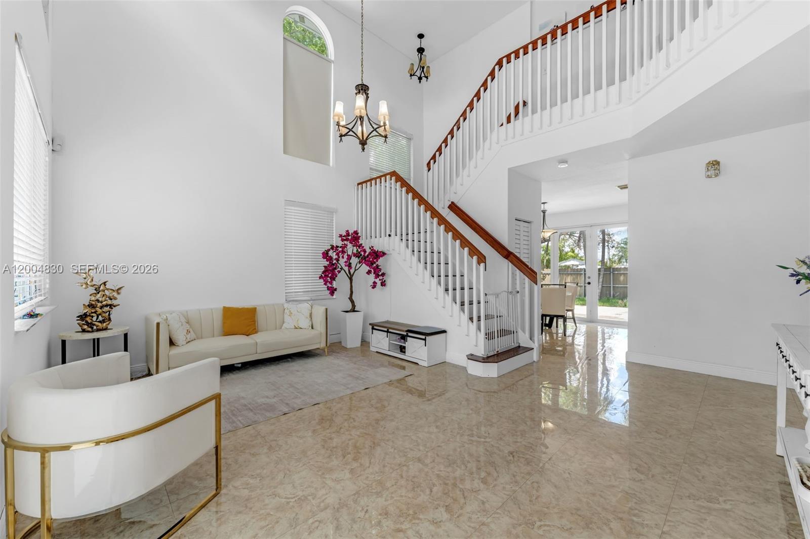 A bright, high-ceilinged foyer features a white staircase, tile flooring, and a chandelier — 13891 SW 39th Ter, Miami FL 33175, MIAMI, FL
