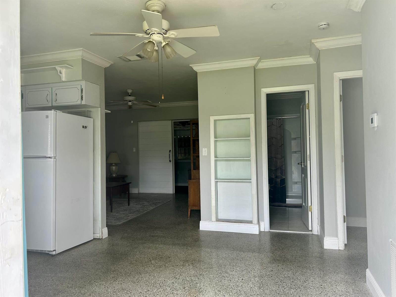 A room with a white refrigerator, ceiling fan, built-in shelving, and a doorway to a bathroom — 3632 NW 25th Avenue, Okeechobee FL 34972, OKEECHOBEE, FL