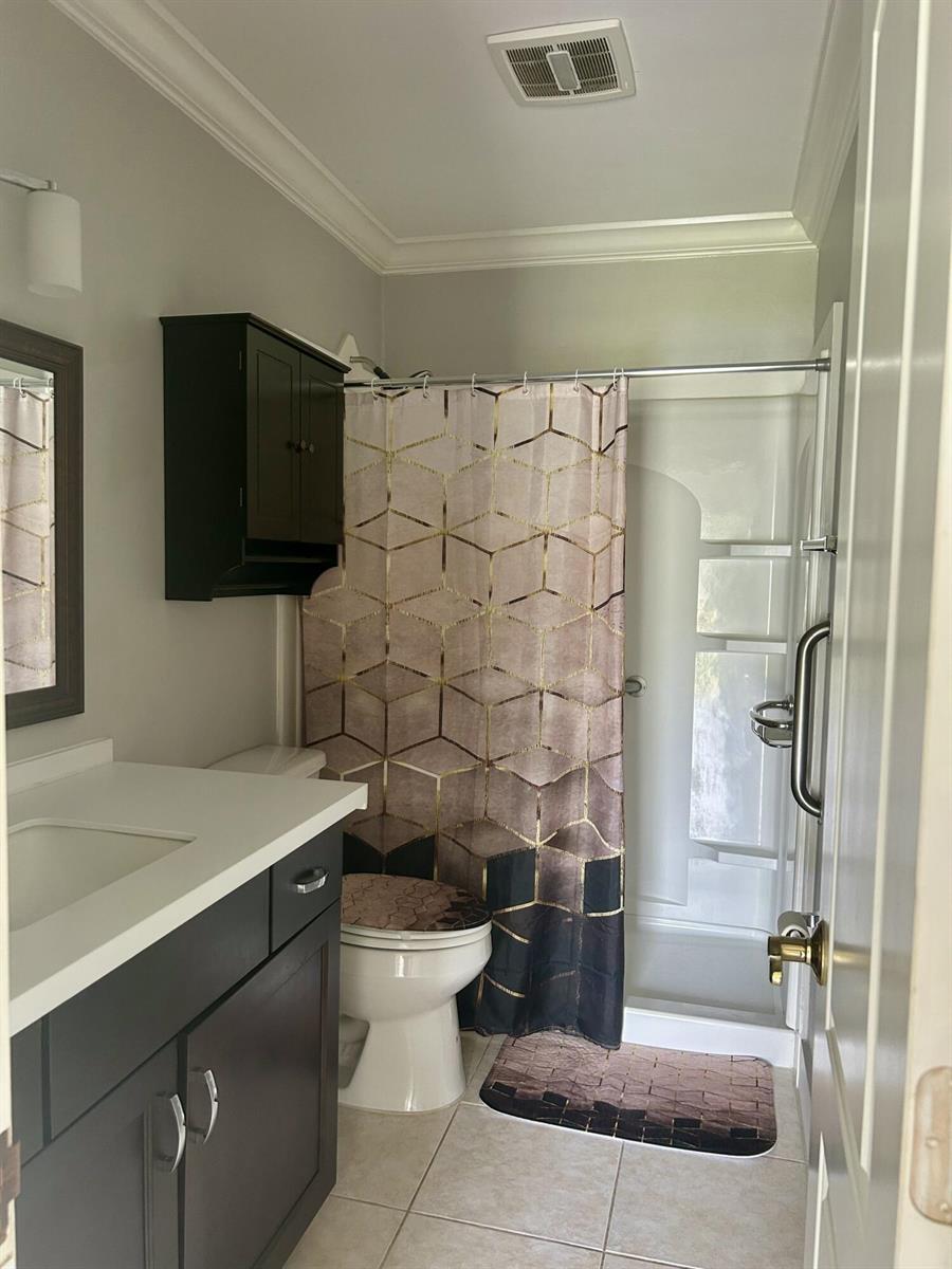 A bathroom features a dark vanity, a toilet with a patterned cover, and a shower stall — 3632 NW 25th Avenue, Okeechobee FL 34972, OKEECHOBEE, FL