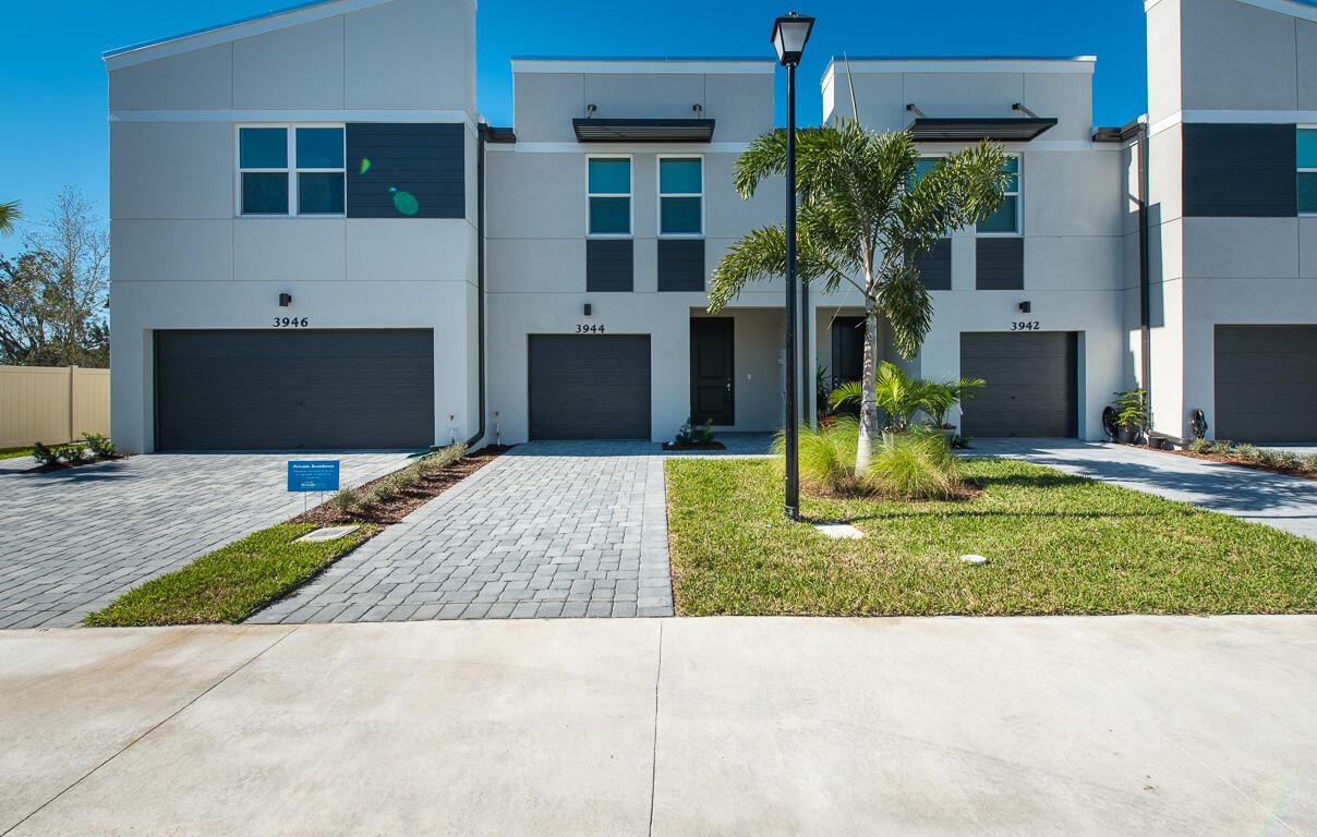A row of modern townhomes with gray garage doors, paved driveways, and small front lawns — 3944 SE Caladium Court, Stuart FL 34997, STUART, FL