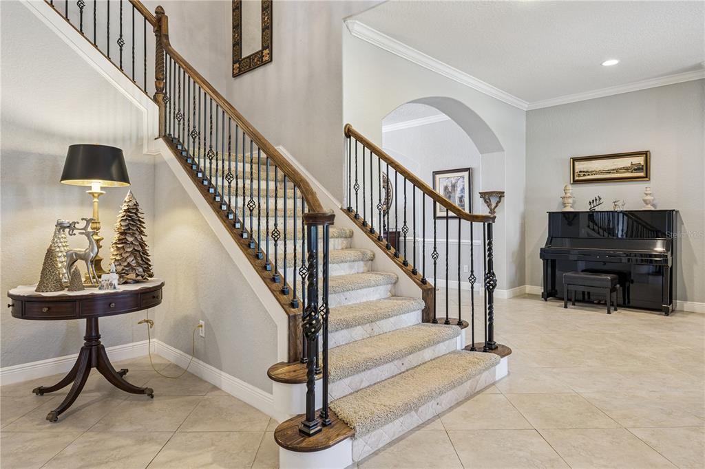 A foyer features a carpeted staircase with wrought iron railings, tile flooring, and a piano — 10327 HART BRANCH CIRCLE, ORLANDO, FL