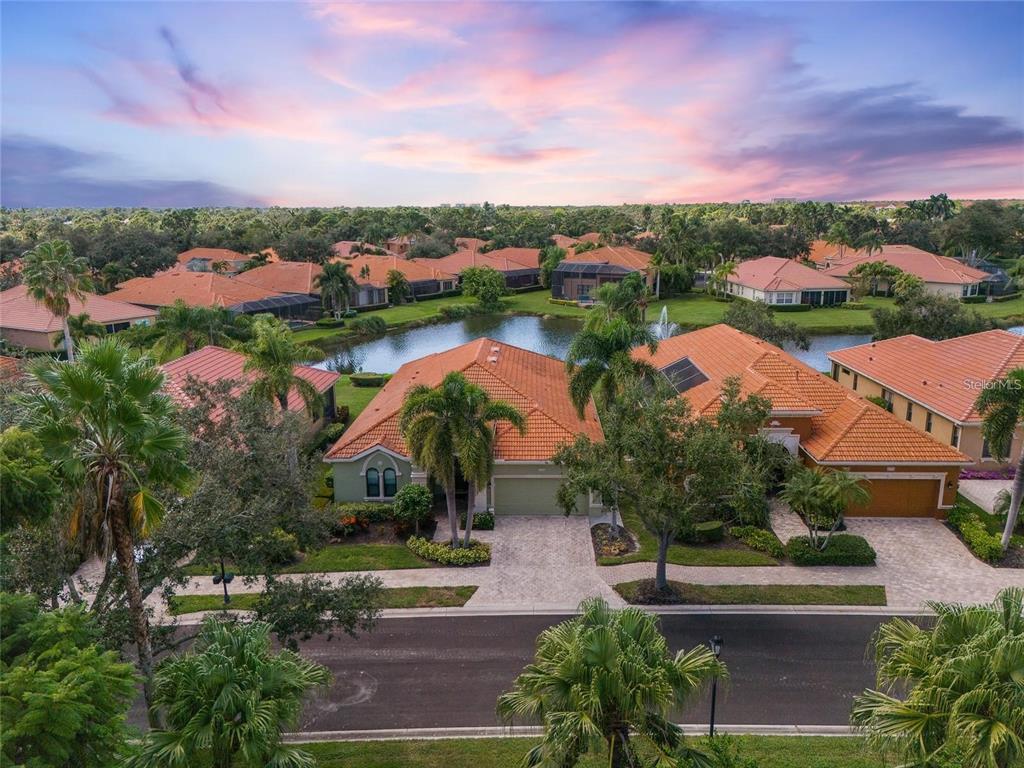An aerial view of suburban houses with orange tile roofs surrounding a central pond — 5175 CANTABRIA CREST, SARASOTA, FL