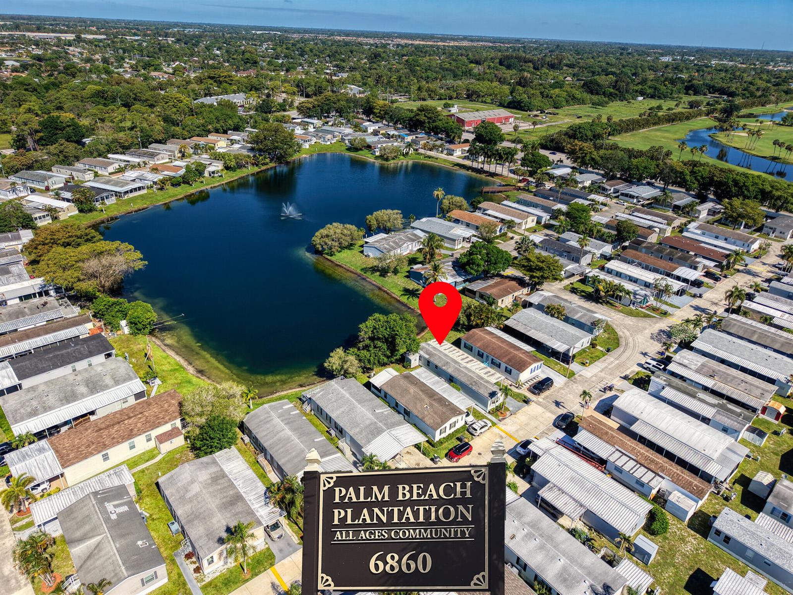 An aerial view shows a mobile home community with a lake and a sign — 153 Plantation Boulevard, Lake Worth FL 33467, LAKE WORTH, FL
