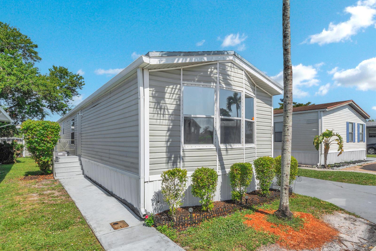 A light gray manufactured home with a concrete walkway and small shrubs in the front yard — 153 Plantation Boulevard, Lake Worth FL 33467, LAKE WORTH, FL