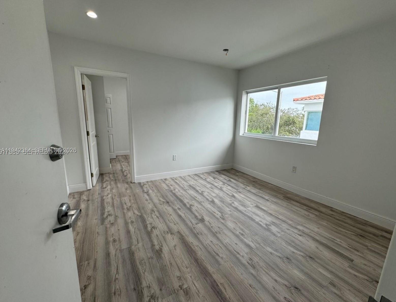 A bedroom with white walls, wood-look flooring, a closet, and a large window — 1248 Marseille Dr # 4, Miami Beach FL 33141, MIAMI BEACH, FL