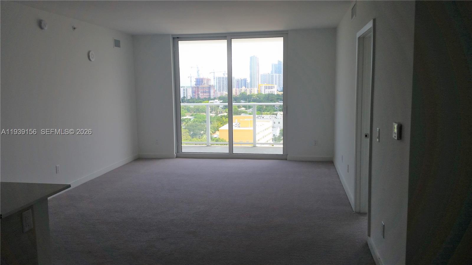 An empty room with beige carpet, white walls, and a sliding glass door to a balcony — 4250 Biscayne Blvd # 1517, Miami FL 33137, MIAMI, FL